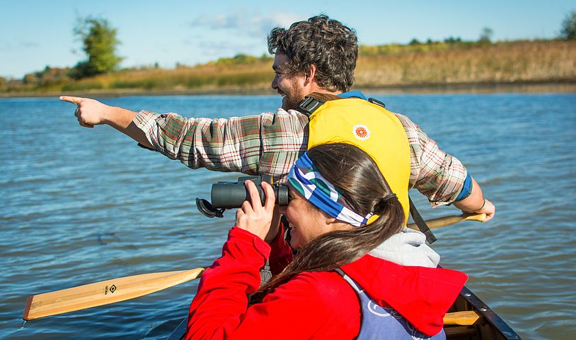 Two paddlers in a canoe viewing wildlife with binoculars.