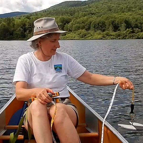 Photo of a woman in a canoe holding a secchi disk into the water