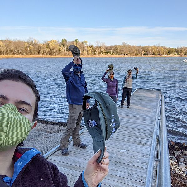 Photo of LCC's Staff and Support Team on a dock taking their hats off to show appreciation for their volunteers.