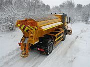 A utility truck spreading salt on a snowy road during winter.